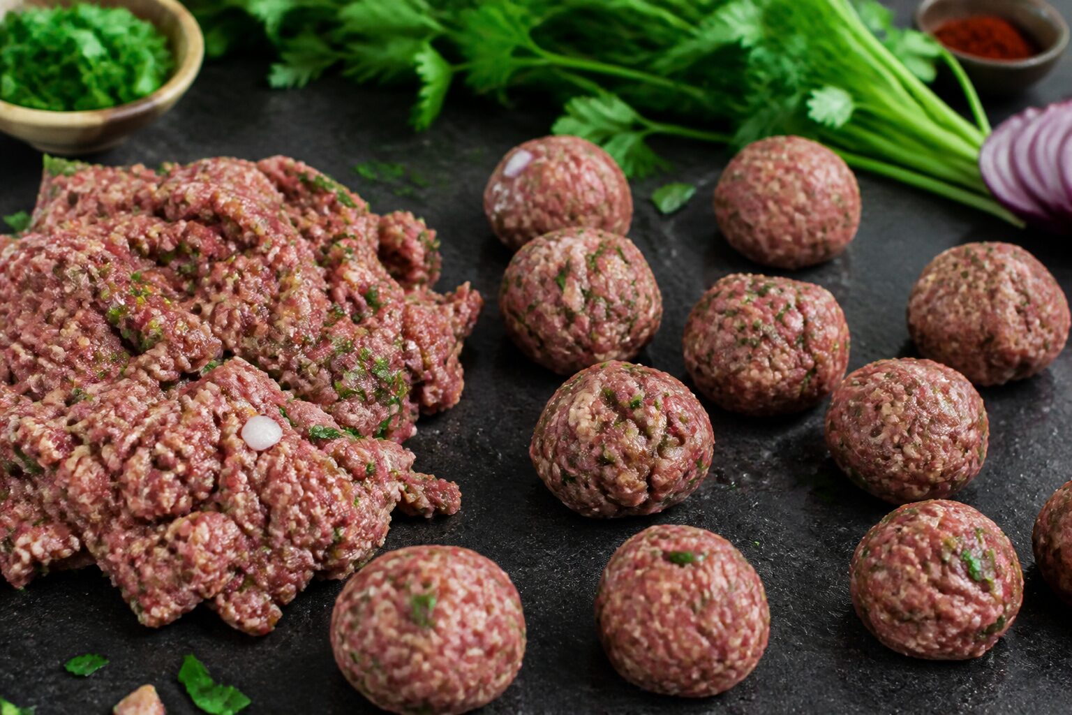 Farce a kefta avec epices et herbes fraiches sur plan de travail, boulettes en cours de facconnage