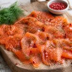 Filet de saumon gravlax maison tranché finement sur planche en bois, avec aneth frais et baies roses