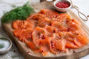 Filet de saumon gravlax maison tranché finement sur planche en bois, avec aneth frais et baies roses