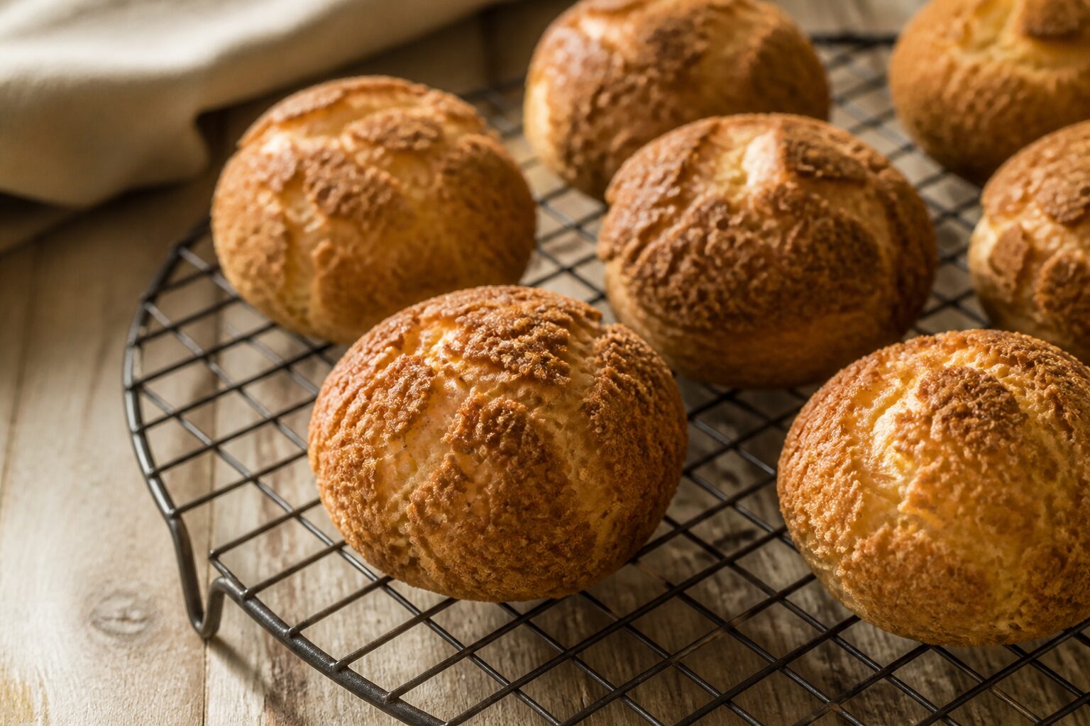 Choux craquelins sortis du four, dorés et croustillants sur une grille, fond bois clair