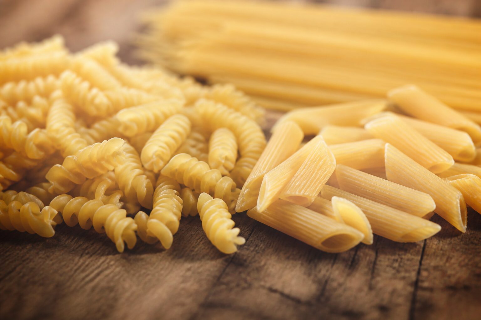 grammes de pâtes cuites par personne : assortiment de pâtes sèches sur planche en bois