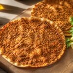 Lahmacun fraichement cuits sur planche, garnis de viande epicee avec citron et herbes