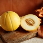 Melon jaune canari entier et coupe sur une planche en bois, lumiere mediterraneenne chaude