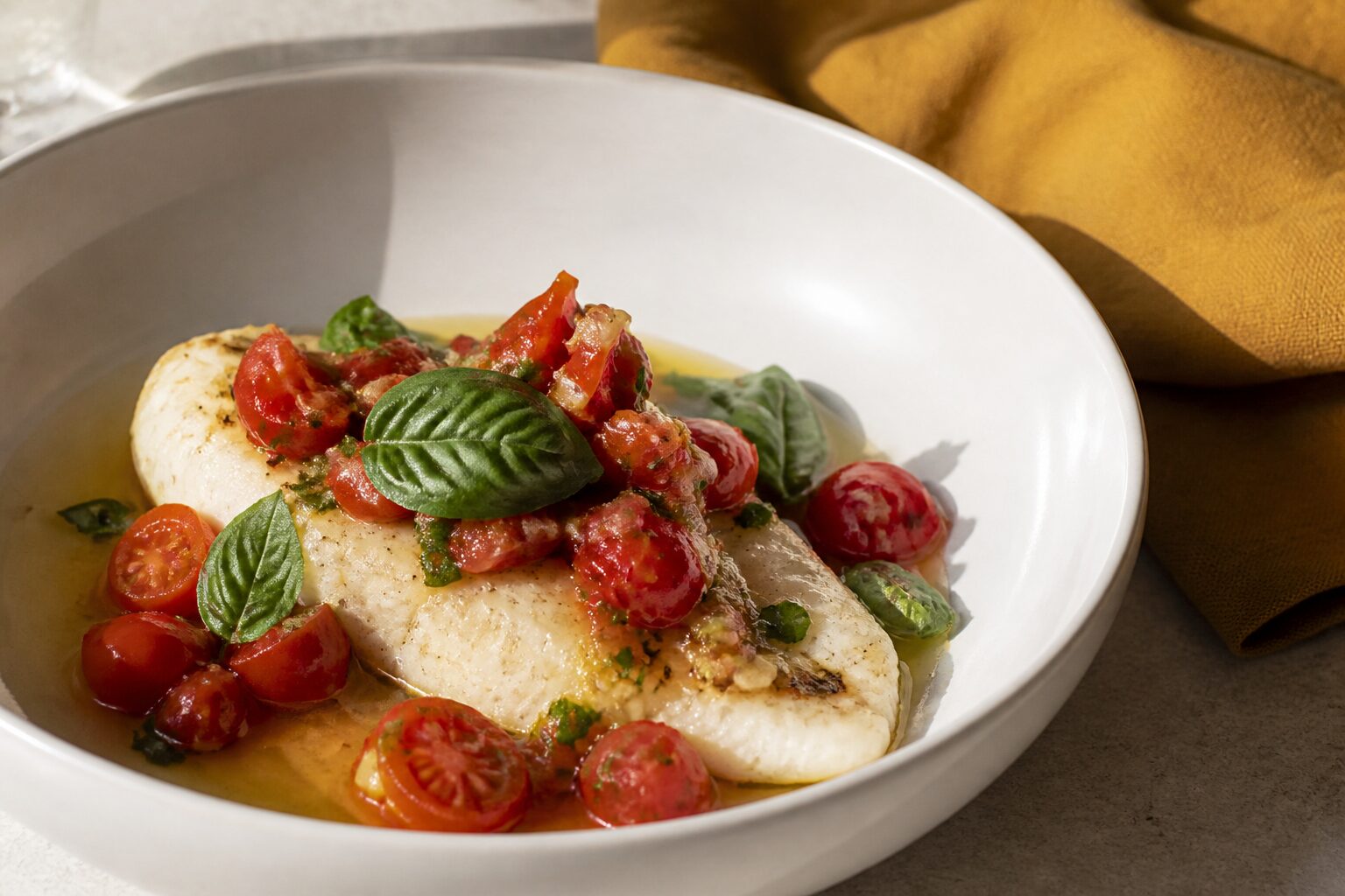 Filet de dorade dressé avec sauce vierge provençale et basilic frais dans une assiette blanche