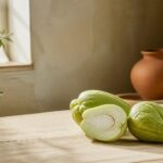 Chayote entière et coupée en deux sur une table en bois clair, lumière naturelle chaude