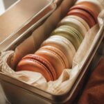 Coques de macarons alignées dans une boîte hermétique sur papier sulfurisé, lumière naturelle chaude