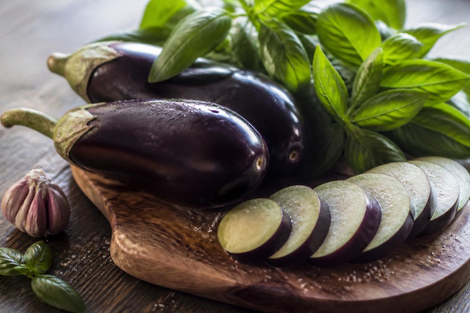 aubergines entières et tranches crues avec ail et basilic sur planche