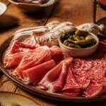 Plateau de charcuterie pour raclette avec jambon cru, saucisson et cornichons sur table en bois