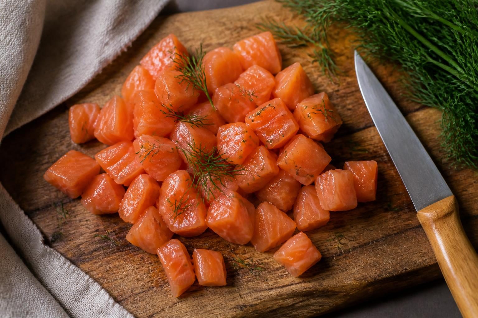 Filet de saumon frais coupé en dés au couteau sur planche en bois