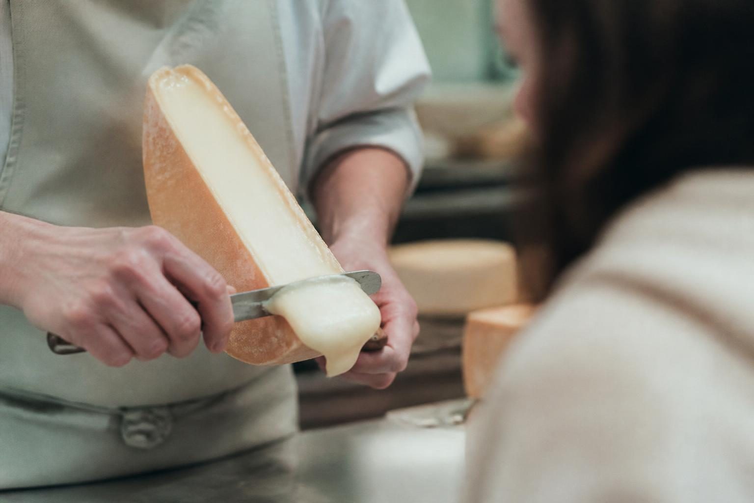 Fromager tranchant une raclette sans lactose en boutique