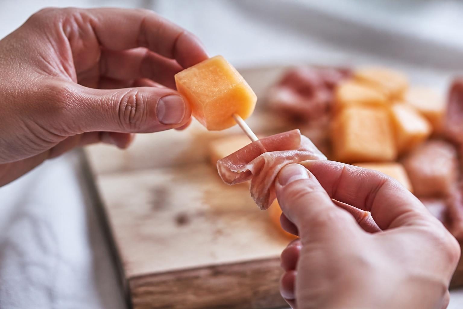 Mains assemblant une brochette apéritive melon et jambon cru