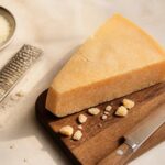 Morceau de parmesan entier posé sur une planche en bois avec râpe et couteau