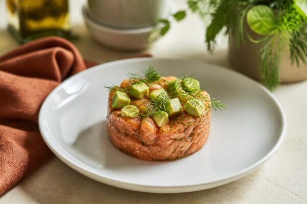 Tartare de saumon frais dressé avec avocat et aneth sur assiette blanche