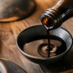 Bouteille de tamari versée dans un bol en céramique sur une table en bois