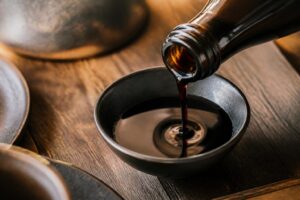 Bouteille de tamari versée dans un bol en céramique sur une table en bois